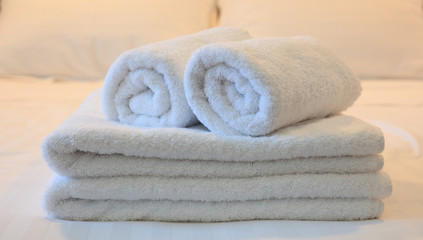 Obraz na płótnie Canvas Hotel bedroom. White rolled and folded towels, white beddings background. Close up view, detail