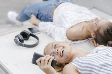 Two happy young women with cell phone and headphones in a skatepark