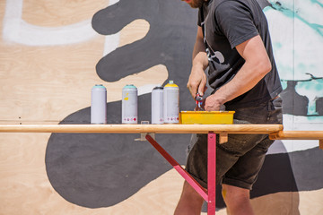 Male graffiti artist making an abstract drawing on wall with spray colors in sunny summer day 