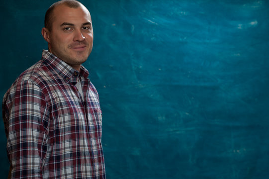 Portrait of young positive man wearing plaid shirt looking at the camera and standing against blue vintage background. Copyspace
