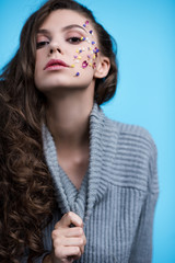 young woman in stylish turtleneck sweater with flowers on face isolated on blue