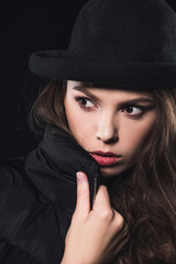 close-up view of beautiful woman in hat and winter jacket looking away isolated on black