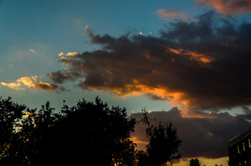 Dramatic cloudscape scene at orange sunset, colored sun lights on the blue sky, fluffy clouds