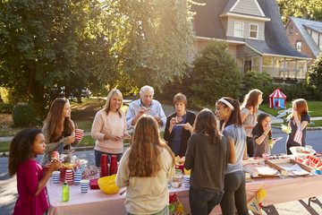 Neighbours talk and eat around a table at a block party - obrazy, fototapety, plakaty