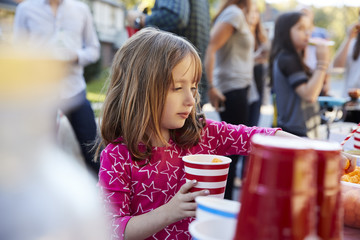 Four year old girl helping herself to food at a block party