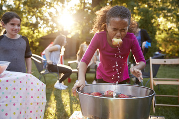Pre-teen girl, apple in mouth, apple bobbing at garden party