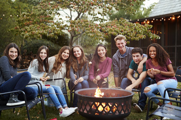 Teenage group sitting around a fire pit smiling to camera