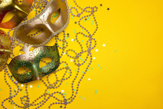 Festive Carnival green and gold masks and beads on a yellow background.