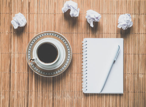 Notepad, pen, crumpled paper and coffee Cup on a bamboo table. The concept of work ideas. Vintage toning.