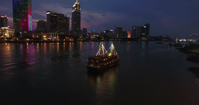 HO CHI MINH CITY, VIETNAM &ndash; MAY, 2016 : Aerial shot of boat moving down Saigon river at night with Hoi Chi Minh cityscape in view