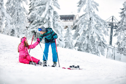 Boy helps to girl to get up from snow with skis