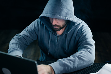 mysterious bearded man in a hood doing something illegal on a laptop