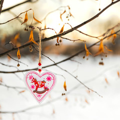 Heart shaped Valentines or Christmas decoration toy hanging on the tree branch with snow on the background