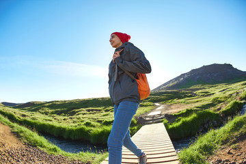 portrait of woman traveler with small orange backpack on a walk in the Valley of the river of Hveragerdi Iceland. Hiking Tour of Reykjadalur Hot Springs