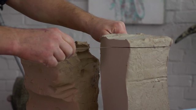 Slow-mo footage. Potter cuts clay with a thread.