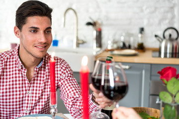 Young happy couple celebrating Valentine's day with a dinner at home drinking wine, cheers.