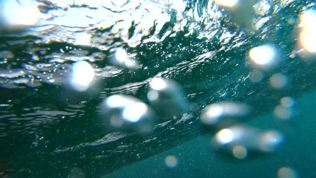 SLOW MOTION, LENS FLARE, UNDERWATER: Big barrel wave rushing towards peaceful rocky tropical island. Camera descends from sunny beaches to deep crystal clear water below a large bubbling ocean wave.