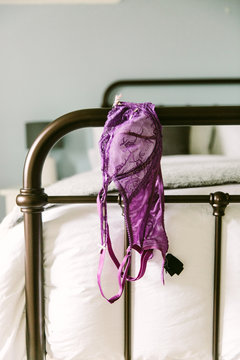 Purple lace bra draped over the end of an iron bedstead