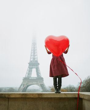 Girl standing on the retaining wall holding heart against Eiffel Tower
