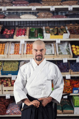A man against the background with racks with fruits and vegetables dressed in Japanese kimono and hakama holding katana. Fruitarianism concept