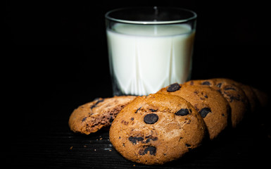 Stack of Chocolate chip cookies and glass of milk on dark wooden background. with copy space.