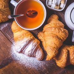 Top view of a cup of tea with a spoon and croissants on the table.