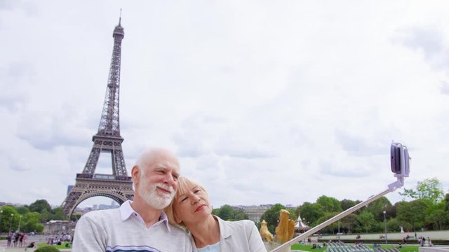 Senior couple near Eiffel Tower in Paris, France doing selfie on mobile with selfie-stick. Smiling tourist traveling in Europe. Active modern life after retirement. Family enjoying time together