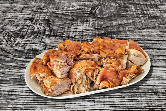 Plateful Of Freshly Spit Roasted Pork Shoulder Slices Served On Porcelain Platter Set On Old Weathered Cracked Pinewood Picnic Table