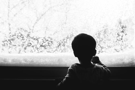 Little kid looking out the window on a snowy day