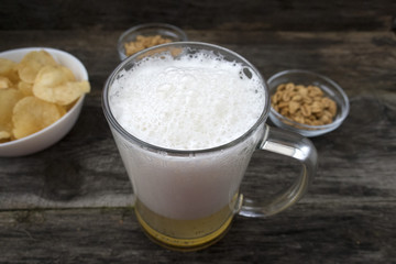 Mug with foam beer, chips and nuts on a wooden background.