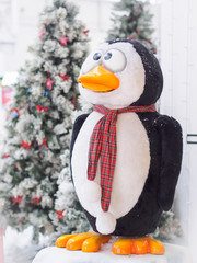 A toy penguin standing against Christmas trees surrounded with gift boxes. Christmas and New Year concept.