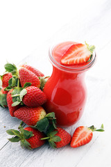 glass of strawberry smoothie and many fresh strawberries on a wooden background.