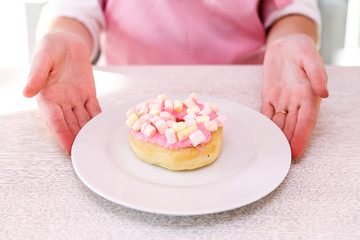 Obraz na płótnie Canvas Female hands holding plate with pink donut on on white wooden background