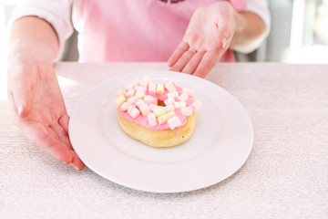 Female hands holding plate with pink donut on on white wooden background