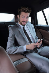 man in suit sitting in car and reading messages on smartphone