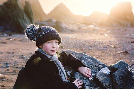 Little girl in a bobble hat on a beach in the early morning.