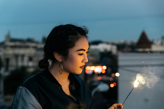 Young woman with sparkler firework in hand on rooftop at dusk