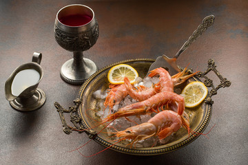 Large tiger Shrimps and slice of lemon fresh in ancient plate full of ice with cooking vane. served with sauce or olive oil and glass of wine