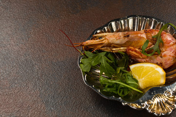 One Fried Tiger Prawn or langostino with greens and Lemon on ancient plate. Close-up view