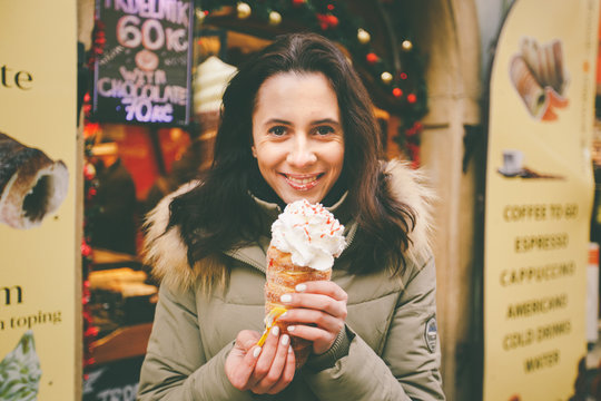 A beautiful girl in a warm jacket eats trdelnik or Trdlo with cream in her hands, in the winter in the Czech Republic, Prague at the Christmas market