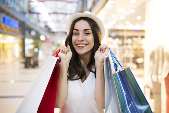 Attractive trendy woman in hat with shopping bags stands at shop in big mall