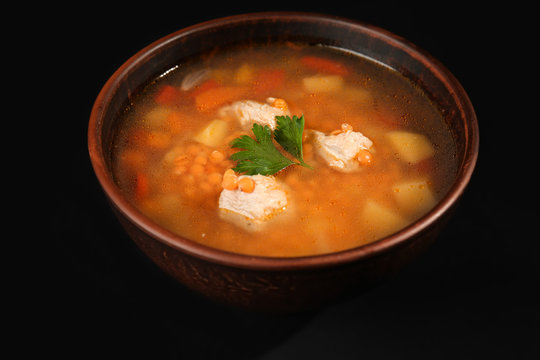 Bowl with tasty lentil soup on black background
