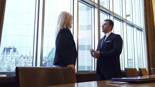 Business man and woman are standing by the panoramic window in their office