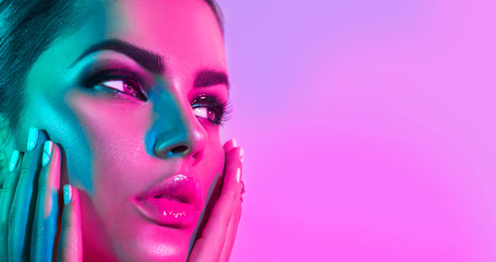 Fashion model woman in colorful bright lights with trendy makeup and manicure posing in studio over...