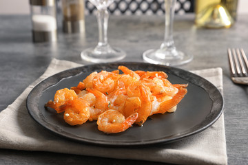Plate with delicious fried shrimps and garlic on table