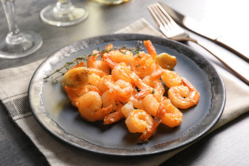 Plate with delicious fried shrimps and garlic on table
