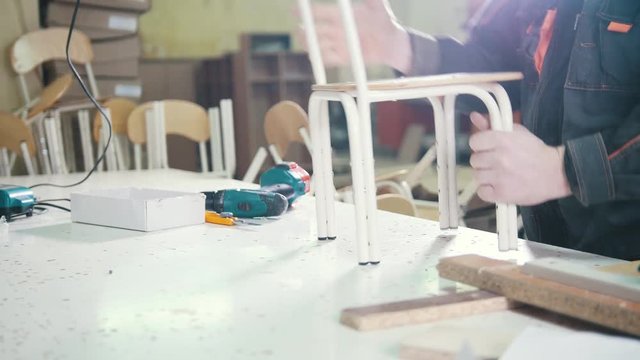Worker man carpenter is screwing chair leg at a furniture factory