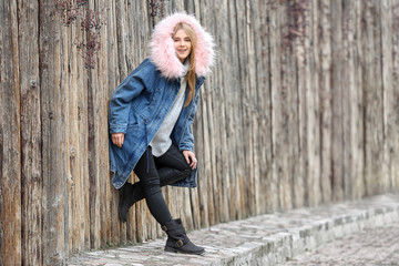 Attractive hipster girl in warm jacket near wooden fence outdoors