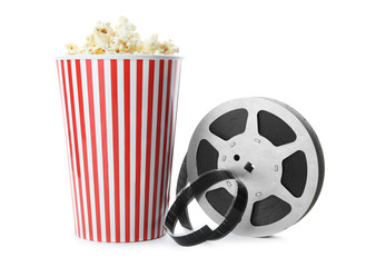 Paper cup with tasty popcorn and movie reel on white background