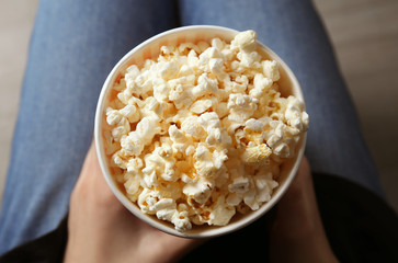 Woman holding paper cup with tasty popcorn, top view